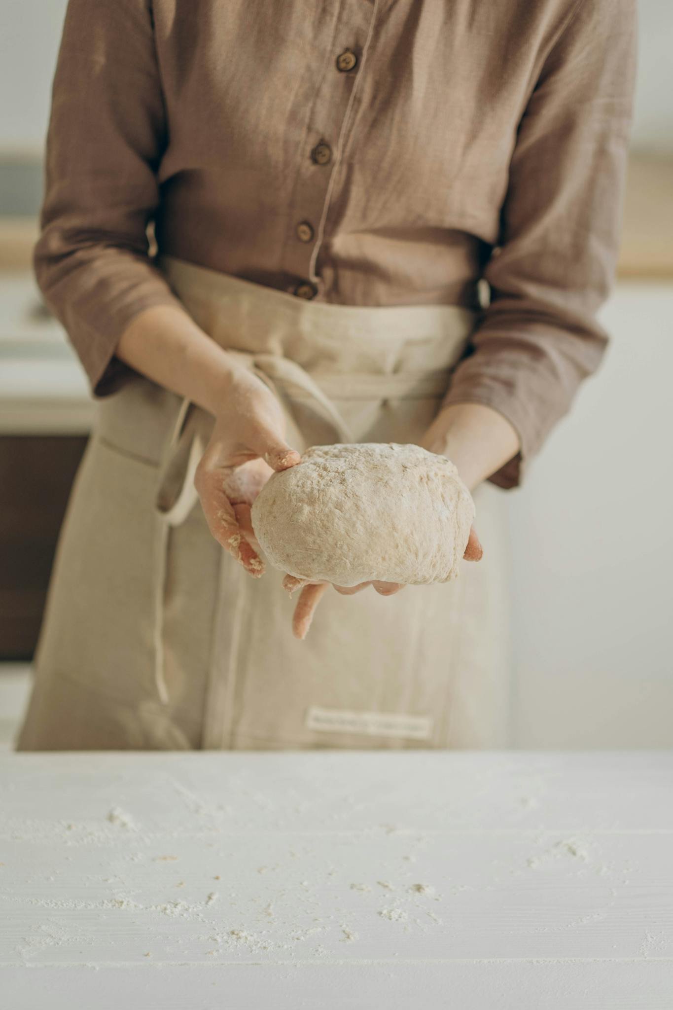A baker in an apron forms fresh bread dough by hand in a cozy kitchen setting.