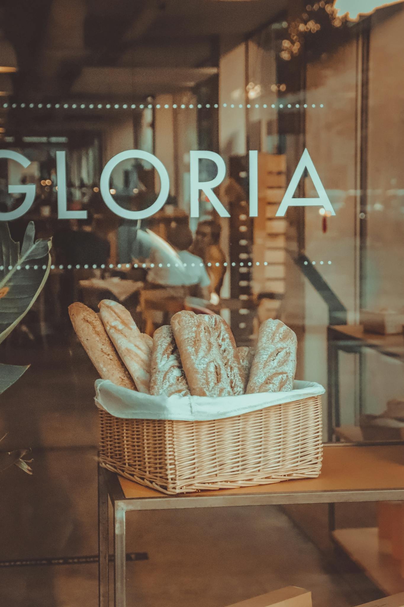 A basket of assorted artisan breads displayed inside a cafe window, evoking a warm, inviting atmosphere.